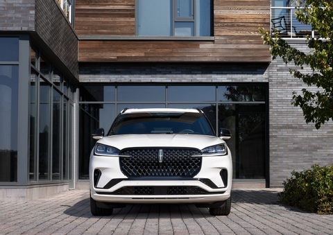 A white 2025 Lincoln Aviator® SUV is shown parked outside a modern building with gray brick and wood accents. | Lincoln of Wayne in Wayne NJ