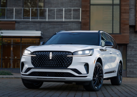 A white 2025 Lincoln Aviator® SUV is shown parked outside a modern building with gray brick and wood accents. | Lincoln of Wayne in Wayne NJ