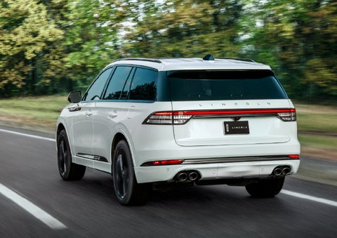A white 2026 Lincoln Aviator® SUV is being driven away down a road lined with colorful trees. | Lincoln of Wayne in Wayne NJ