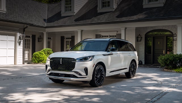 A white 2026 Lincoln Aviator® SUV is parked in the driveway of a luxury home. | Lincoln of Wayne in Wayne NJ