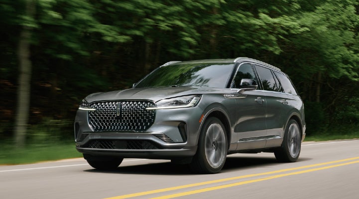 A 2027 Lincoln Aviator® SUV is being driven down a road lined with trees. | Lincoln of Wayne in Wayne NJ