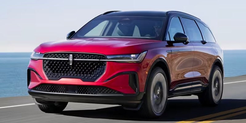 A red Lincoln Star EV concept SUV drives down a coastal road, with the ocean visible in the background.