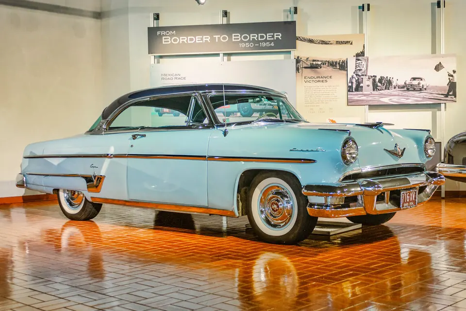Light blue vintage Mercury coupe with a black roof and white wall tires, on a shining brown tiled floor.