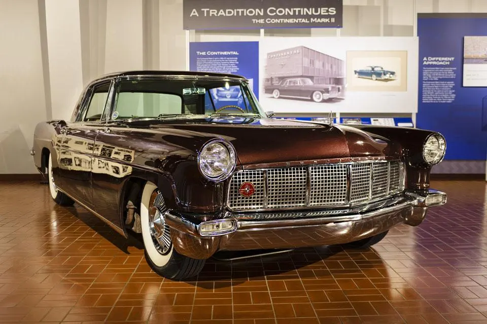 A classic, deep red Continental Mark II car with a large chrome grille and whitewall tires on a tiled floor.