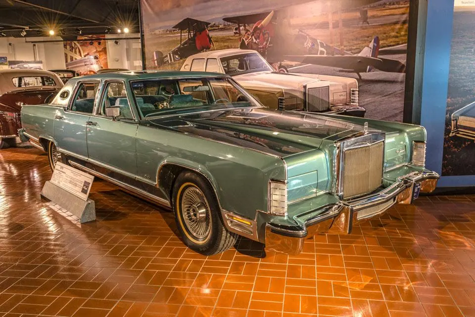 A light green 1970s Lincoln Continental sedan with a prominent chrome grille on a reddish-brown tiled floor.